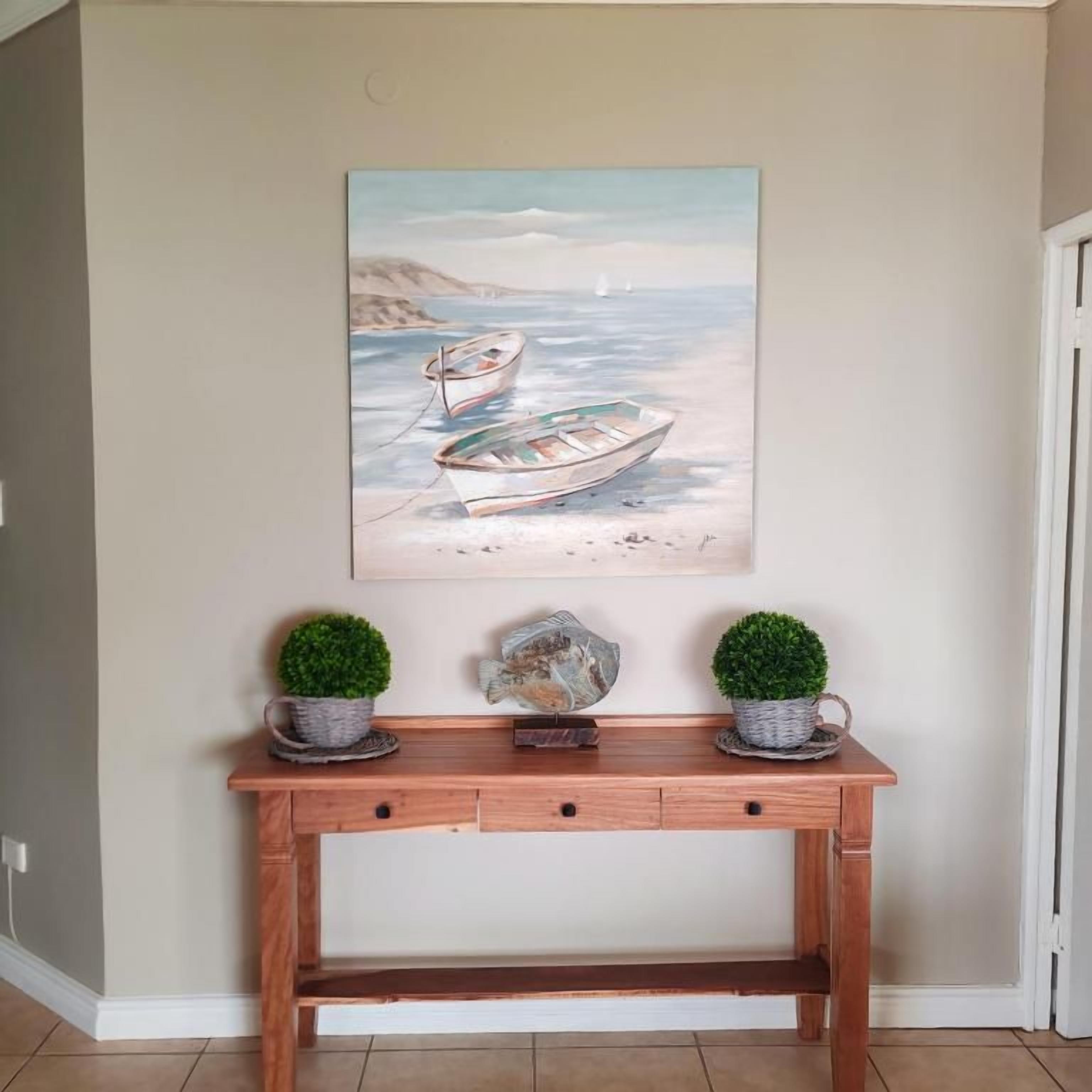 A wooden console table with two potted plants and a painting of boats on water.