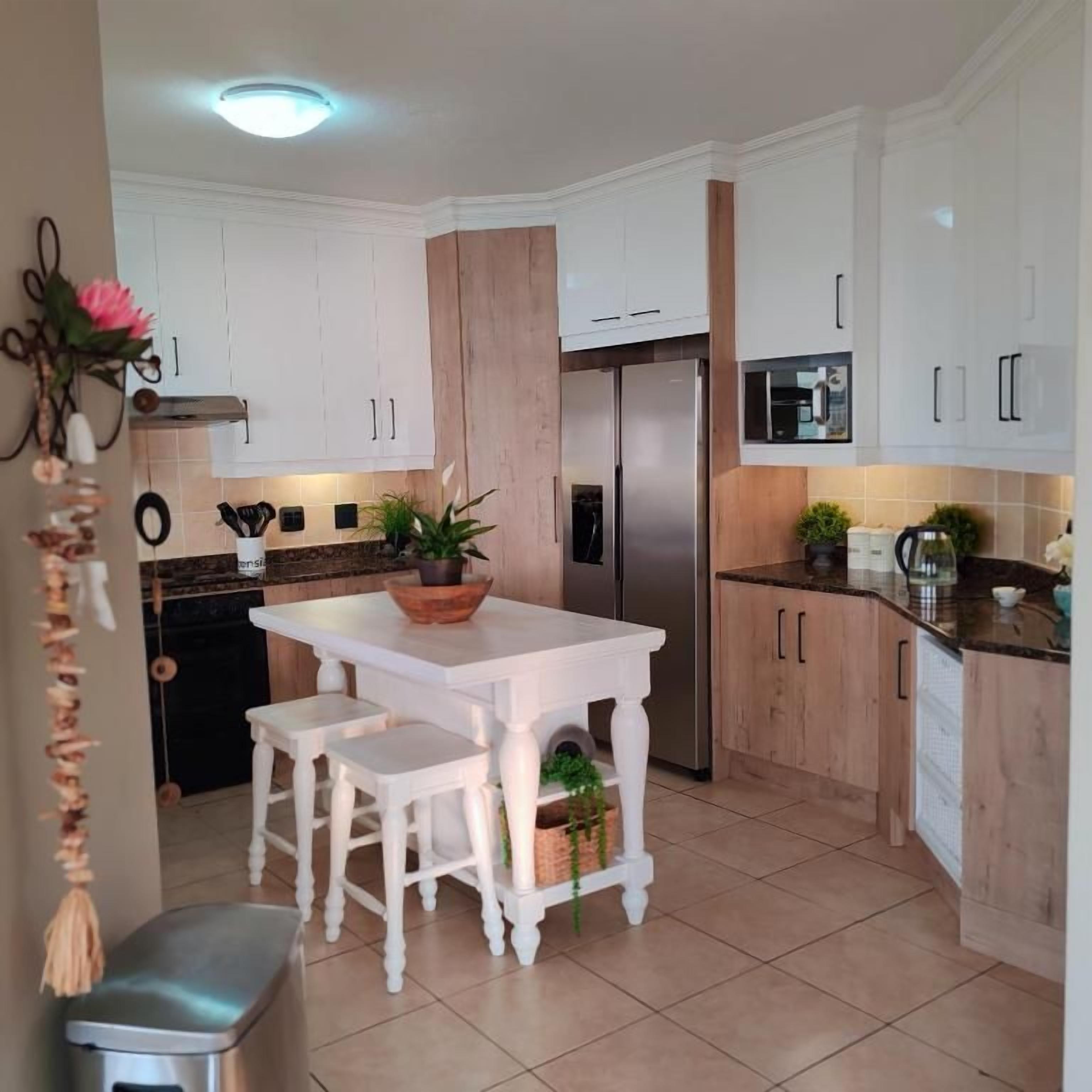 Una cocina con armarios blancos, una isla central con taburetes, un refrigerador de acero inoxidable y un microondas.