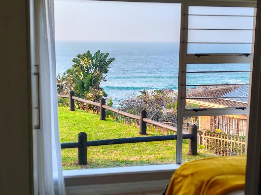 A room with a view of the ocean through a window with a wooden railing.