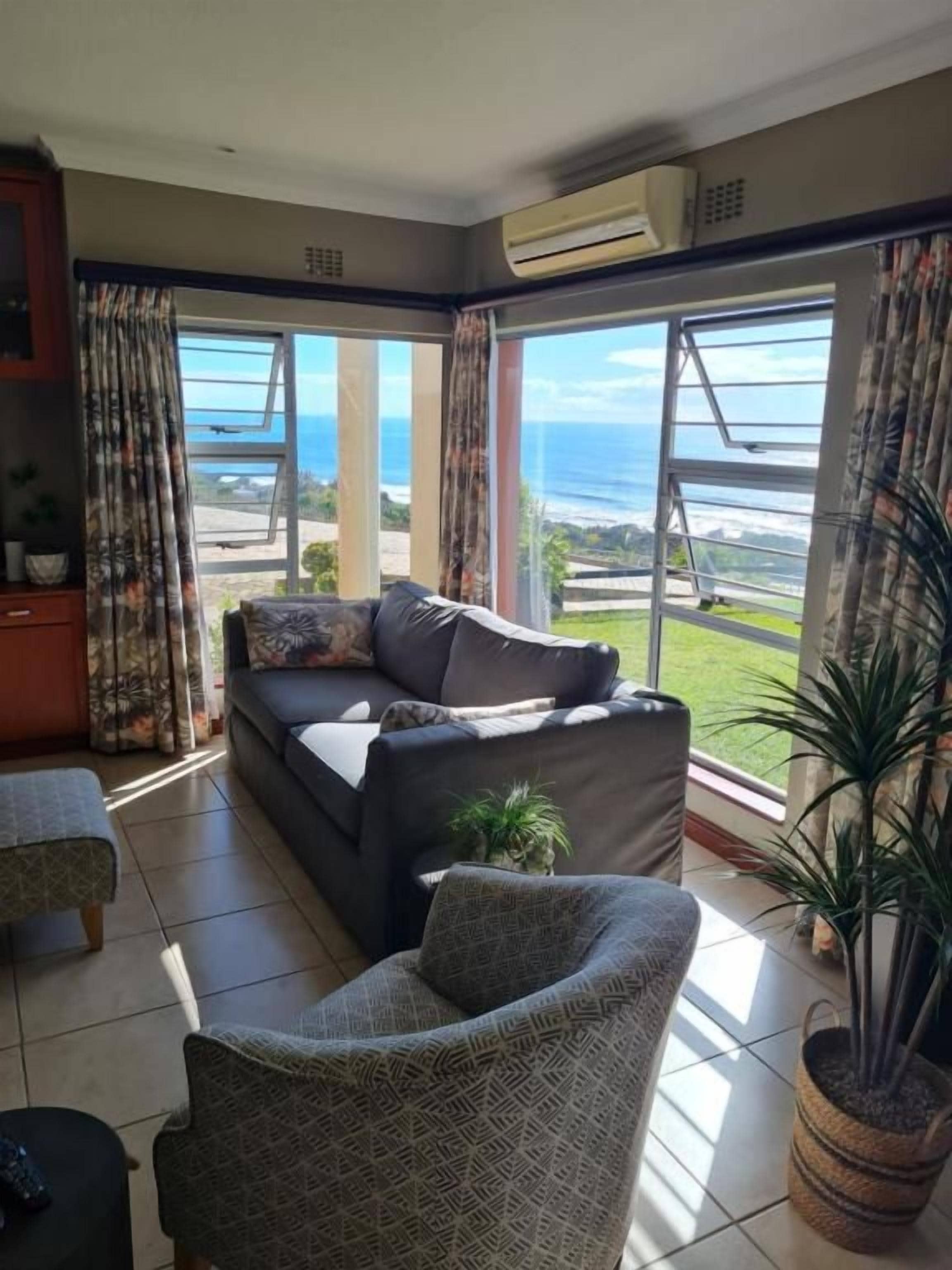 A living room with a sofa, armchairs, and a view of the ocean.