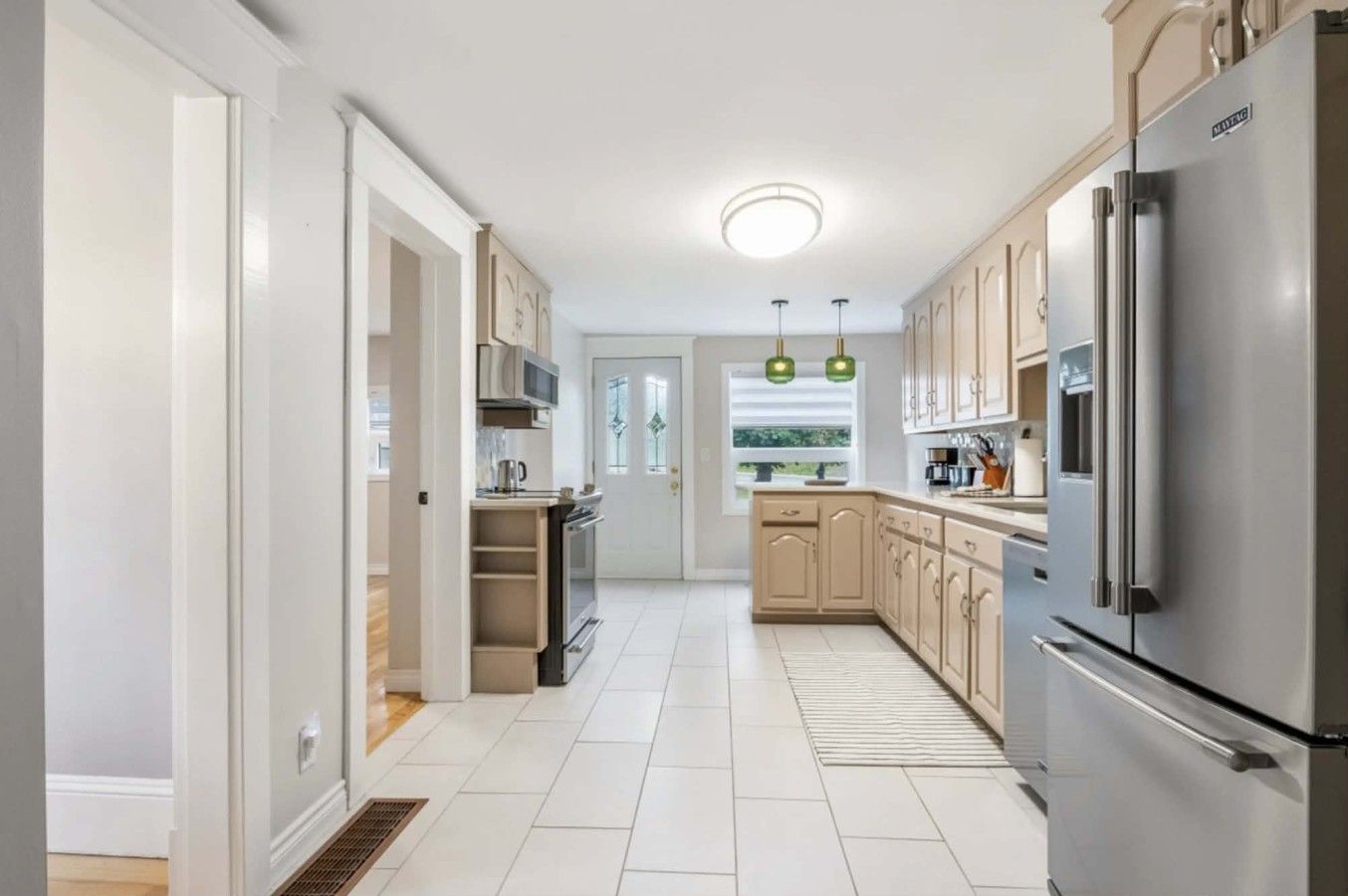 A modern kitchen with a stainless steel refrigerator, beige cabinets, and a window with a view.