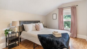 A bedroom with a bed, bedside tables, a lamp, a window with curtains, and a view of greenery outside. - 3-Bedroom Stay near Hostpitals (Moncton)
