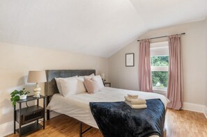 Camera da letto con un letto, comodini, una lampada, una finestra con tende e vista sul verde.