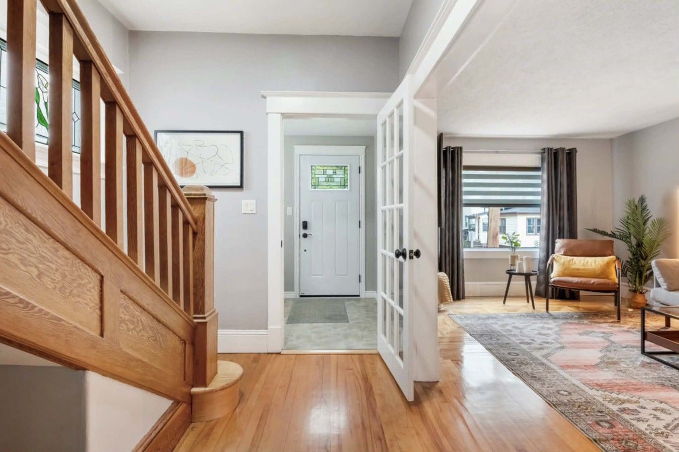 A wooden staircase leading to a door, a living room with a patterned rug, a leather armchair, and a view of the outside.