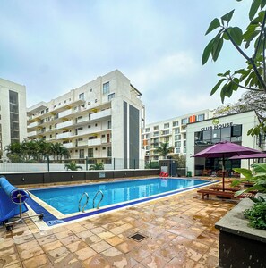 Piscina com deck ladrilhado, rodeada por um edifício com várias andares, varandas e placa indicando Club House.