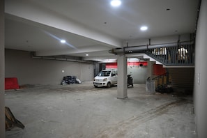 A spacious indoor area with a white van parked in the center, a staircase on the right, and a red barrier on the left.