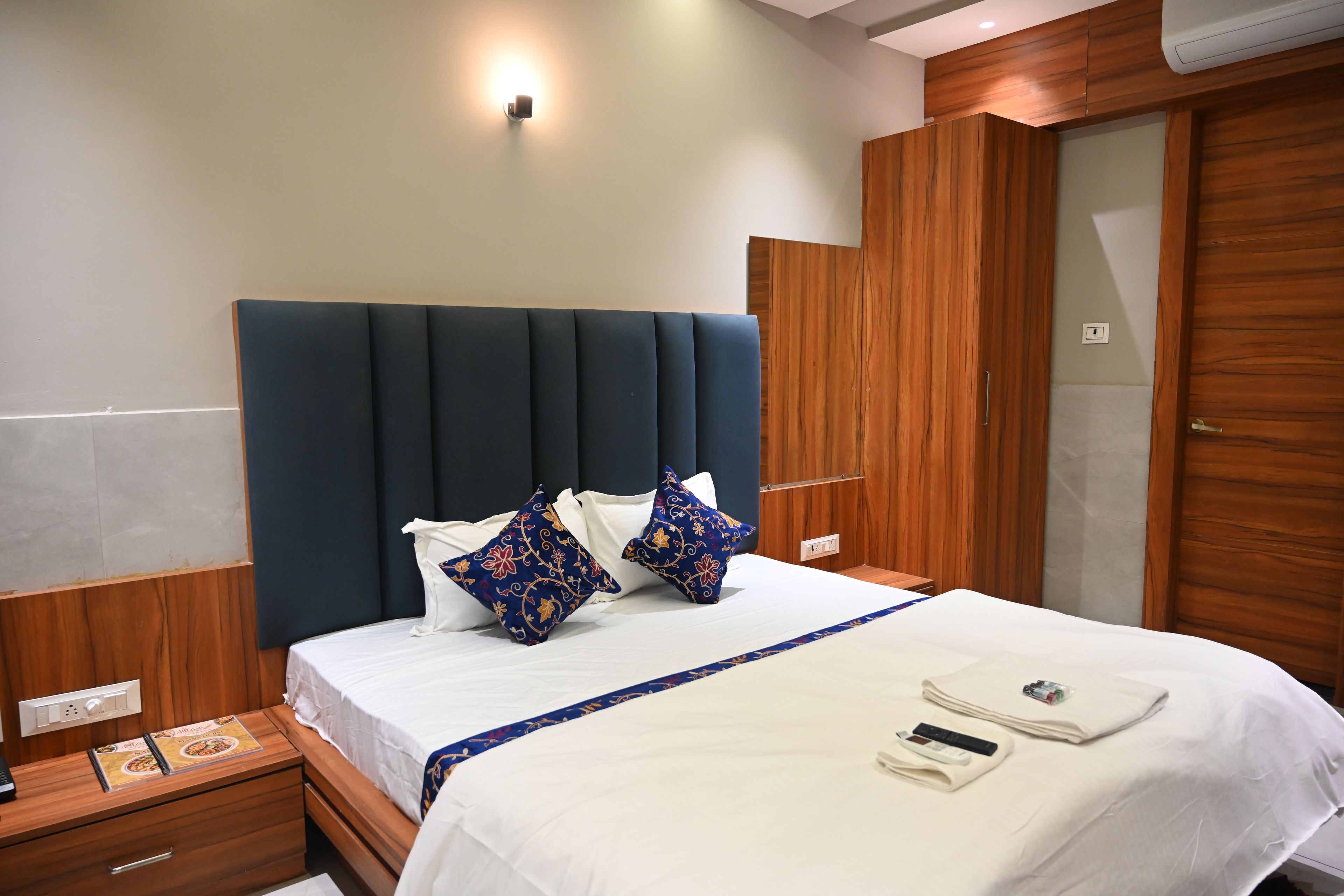 Habitación de hotel con una cama grande, armario de madera, mesita de noche y lámpara de pared.