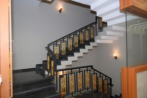 A staircase with black railings and golden accents, leading to a landing with a glass partition. - SHREE LEELA HOTEL AND RESTAURANT (Tarana)