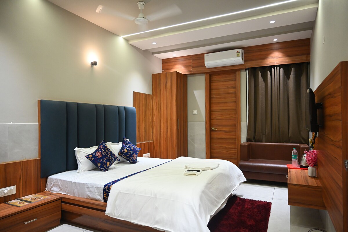 A modern bedroom with a large bed, bedside tables, a built-in wardrobe, a seating area, and a flat-screen TV.