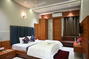 A modern bedroom with a large bed, bedside tables, a built-in wardrobe, a seating area, and a flat-screen TV.