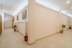 Un couloir au sol carrelé, agrémenté de plantes en pot et orné de tableaux encadrés sur les murs.