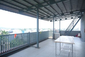 A covered balcony with a view of buildings, a metal table, and a trash bin.
