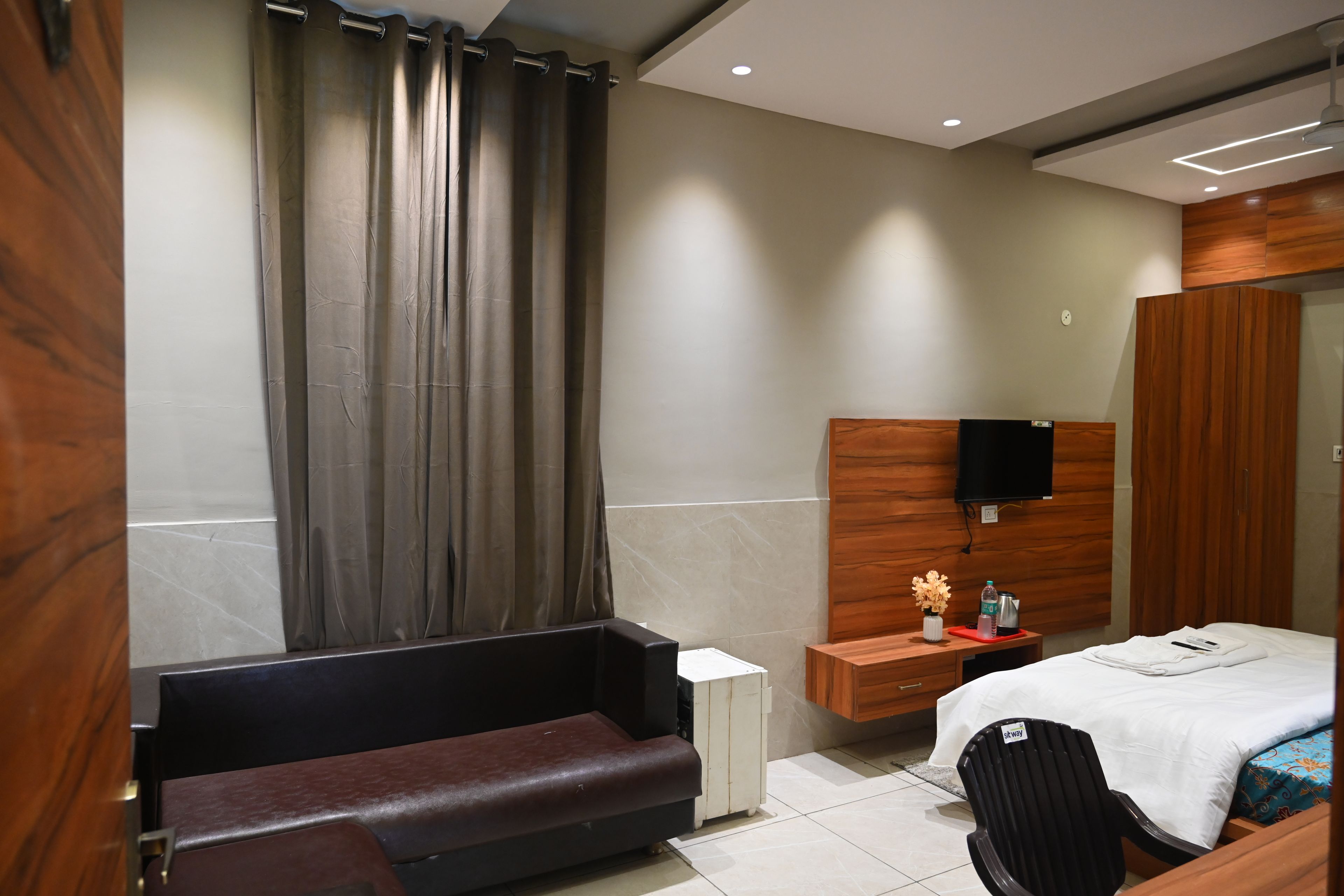 Een moderne hotelkamer met een bed, een bankje, een televisie en een kleine tafel met een vaas.