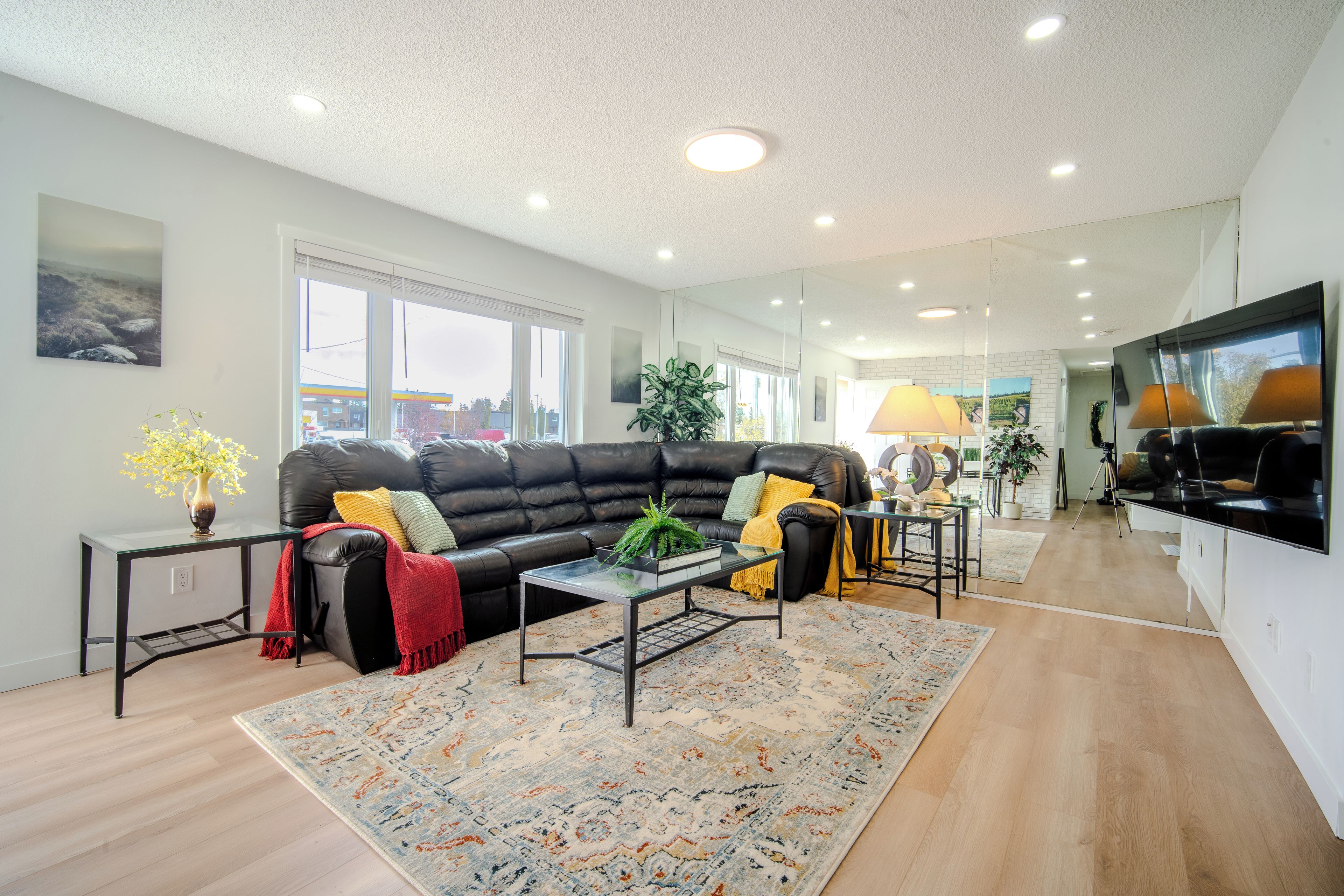 A modern living room with a black leather sofa, a glass coffee table, and a patterned rug.
