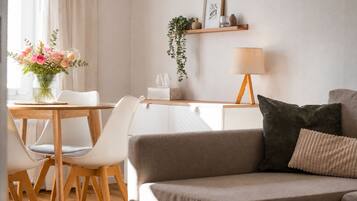 Ein modernes Wohnzimmer mit einer Couch, einem Esstisch mit Stühlen, einer Lampe und einem Blumenstrauß.