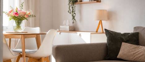 Un salon moderne avec un canapé, une table à manger et des chaises, une lampe et un vase de fleurs.