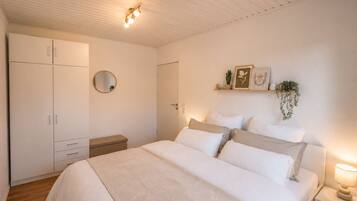 Ein Schlafzimmer mit einem Bett, Nachttischen, einem Kleiderschrank, einem Spiegel und an der Wand befestigten Regalen mit Pflanzen.