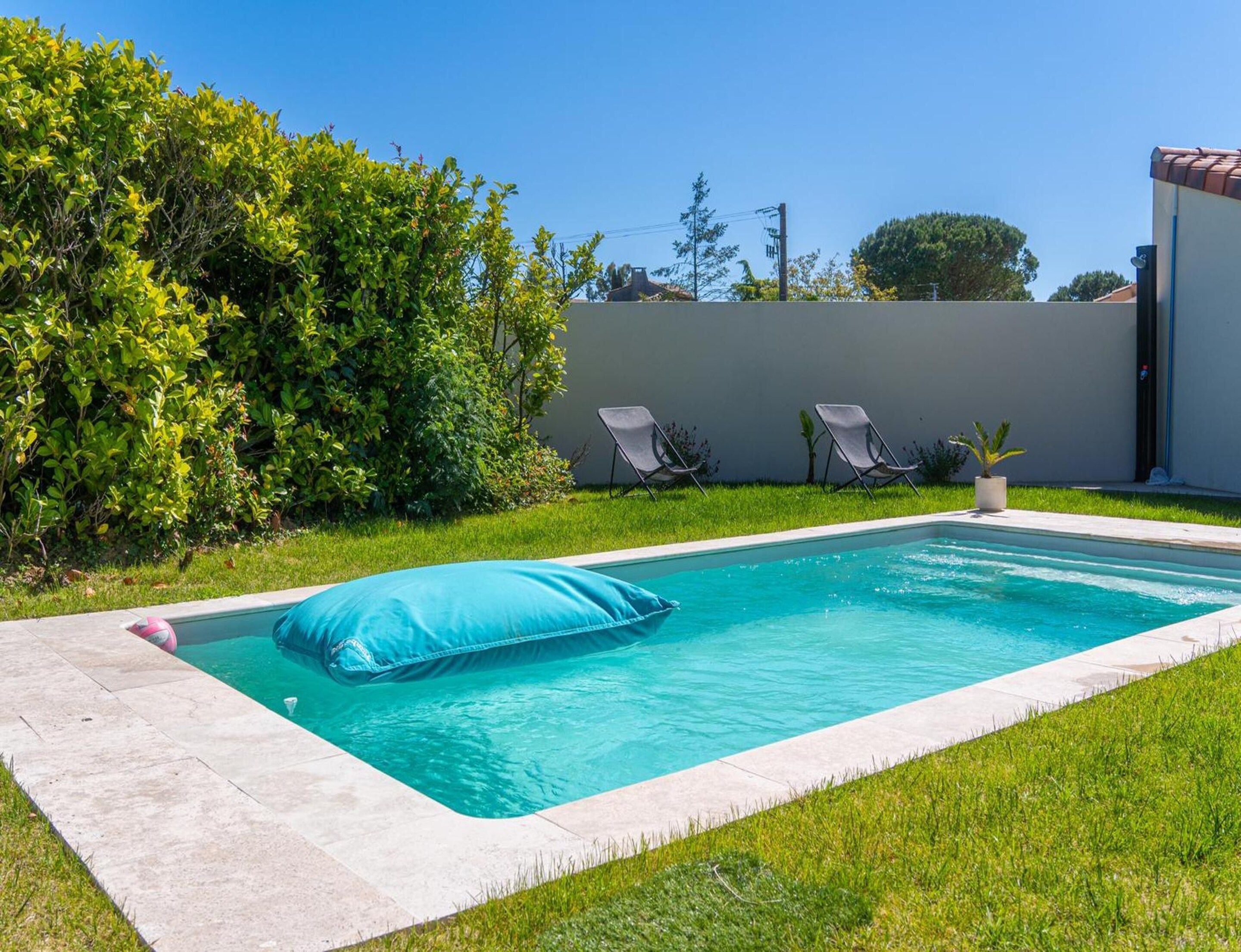 A rectangular swimming pool with a blue cushion, surrounded by a grassy area and a low wall.
