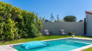 Una piscina rectangular con un cojín azul, rodeada por un césped y un muro bajo.