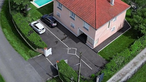 Un edificio de dos pisos con techo de tejas rojas, piscina y zona de estacionamiento con dos autos.