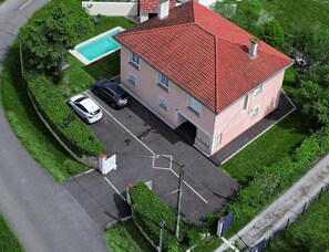 Edifício de dois andares com telhado de telhas vermelhas, piscina e área de estacionamento com dois carros.