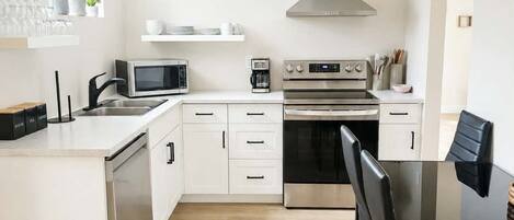 A modern kitchen with white cabinetry, a stainless steel range, a microwave, and a coffee maker.