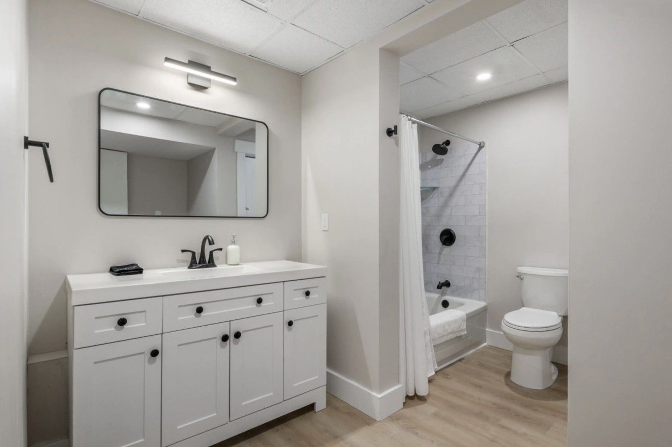 A modern bathroom with a white vanity, a large mirror, a shower with a glass door, and a toilet.