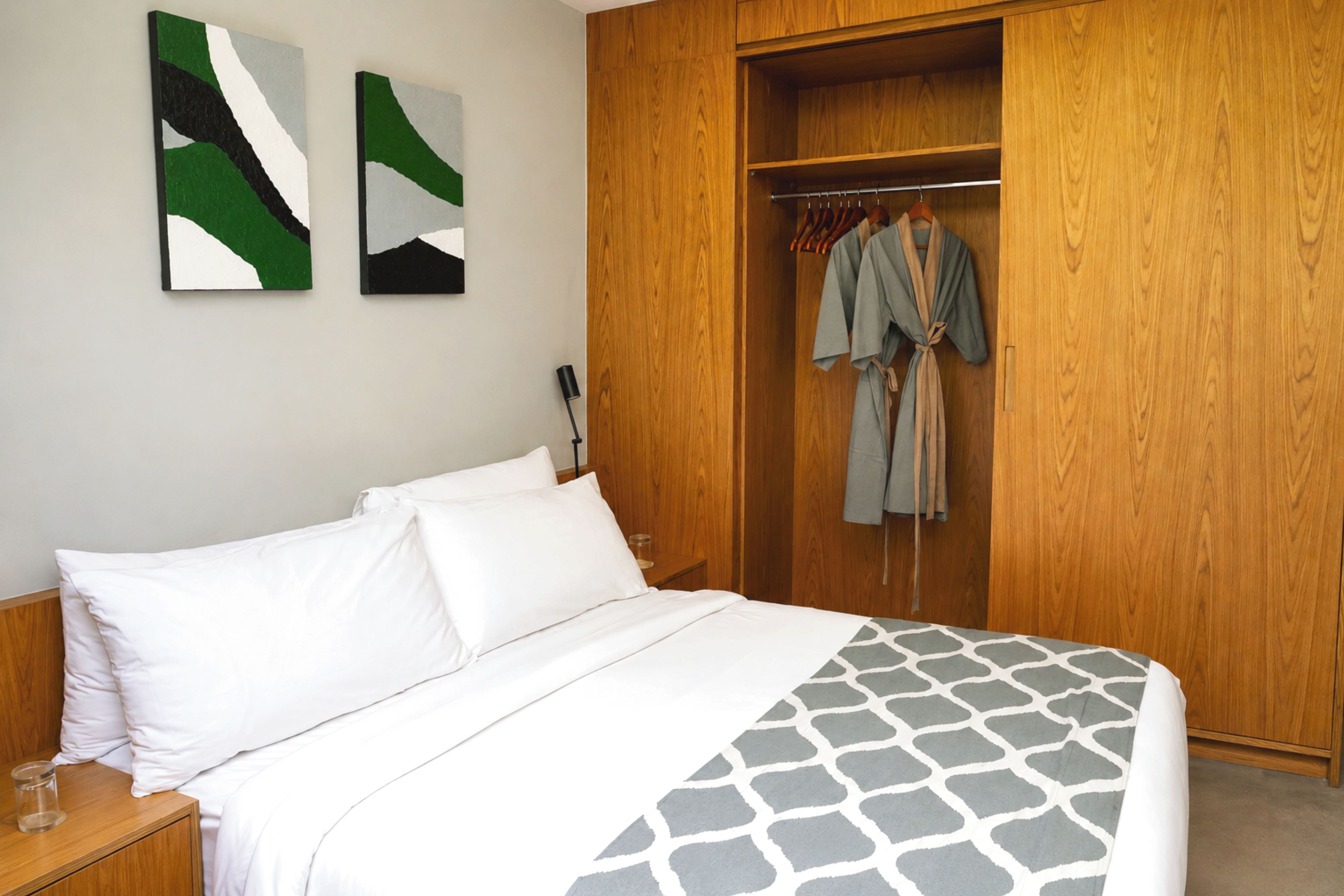 Ein Schlafzimmer mit einem Bett, einem Holzschrank und zwei abstrakten Bildern an der Wand.