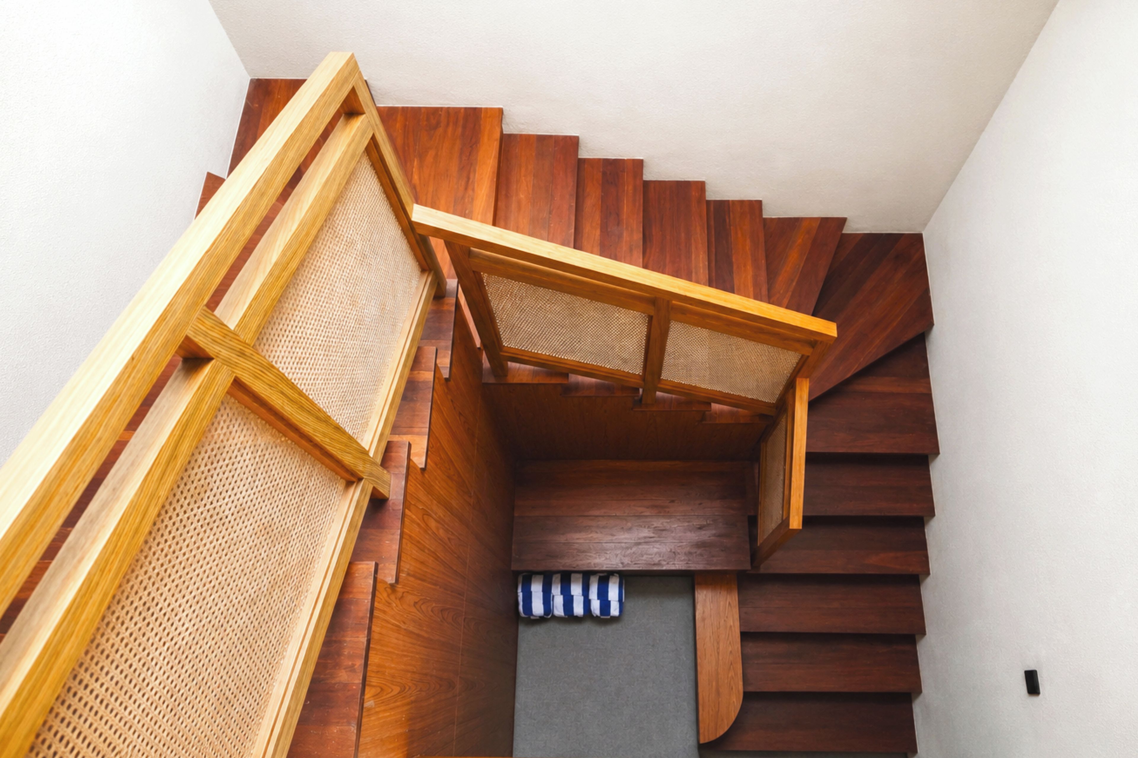 A wooden staircase with a woven handrail and a blue-striped rug at the bottom.
