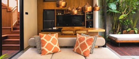 A modern living room with a sofa, two decorative pillows, a coffee table, and a kitchen area with copper pendant lights.