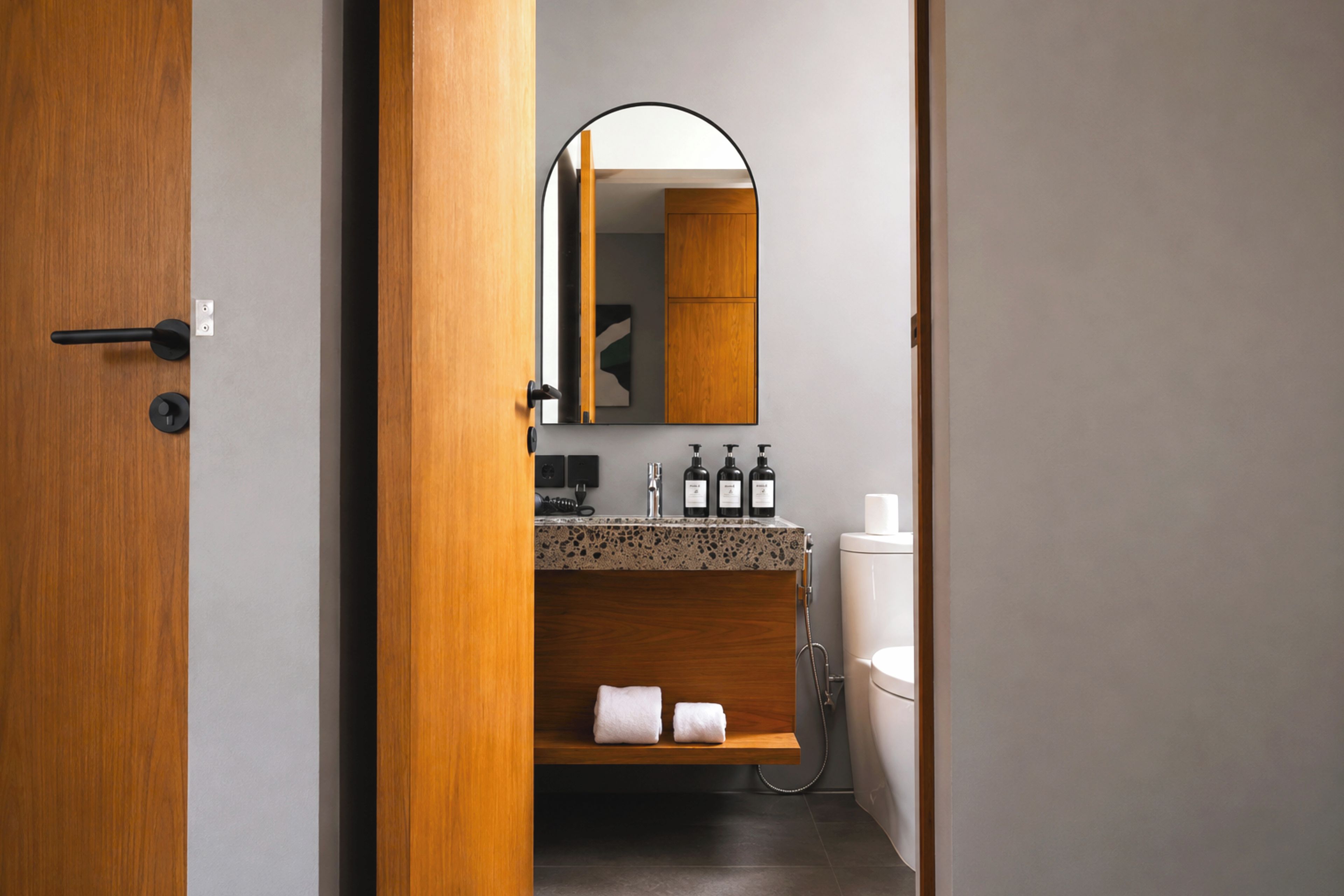 A modern bathroom with a wooden door, a mirror, a sink with a granite countertop, and a toilet.
