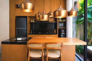 A modern kitchen with wooden cabinets, a black countertop, and a central island with two chairs. - Villa Daksa Ubud by Tasvan (Gianyar)