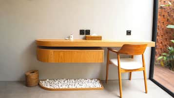 A modern bathroom with a wooden vanity, a chair, a small basket, and a pebble tray.