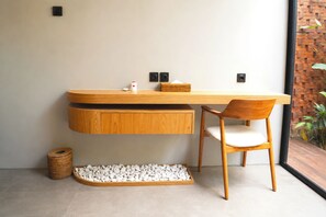 Un baño moderno con tocador de madera, una silla, una cesta pequeña y una bandeja con guijarros.
