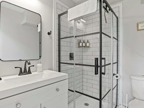 Un bagno moderno con doccia vetrata, lavandino bianco con rubinetto nero e specchio sopra il lavandino.