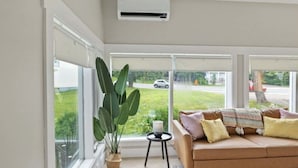 Een moderne woonkamer met een bank, een plant in pot en grote ramen.