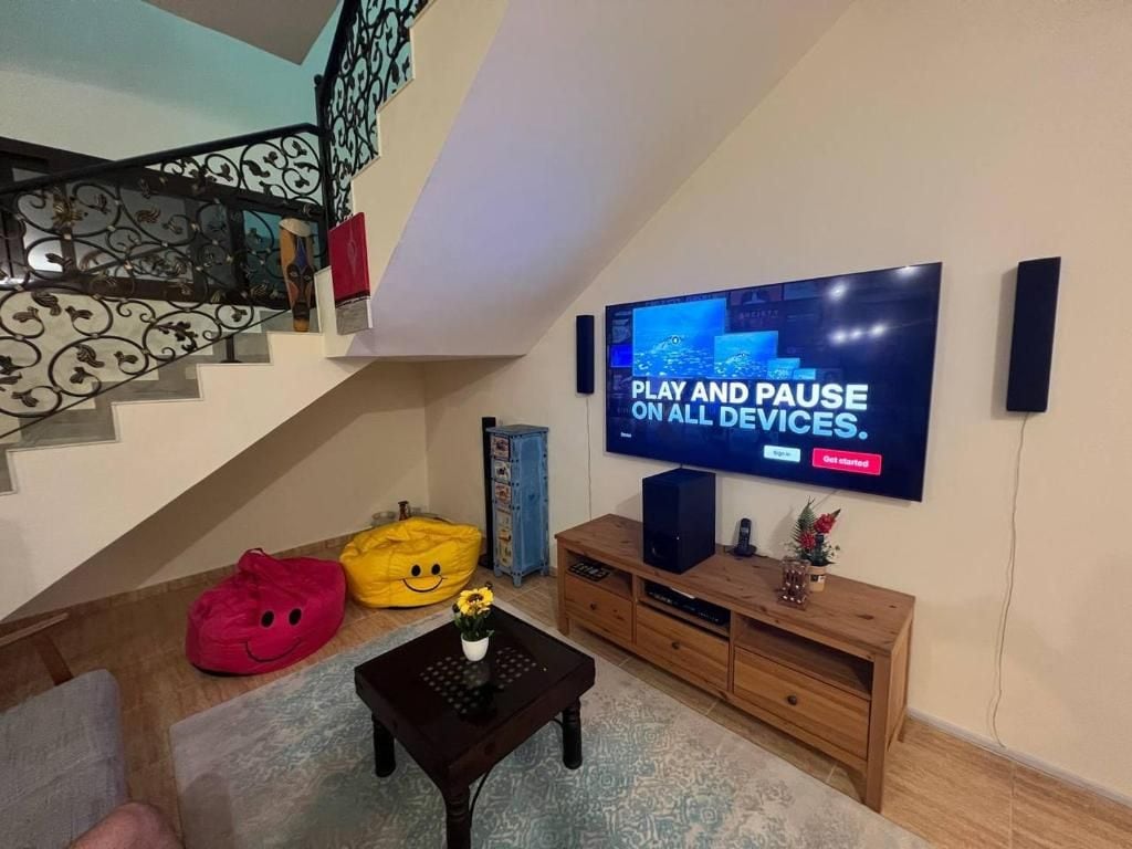 Een woonkamer met een flatscreen televisie aan de muur, een trap met decoratief hekwerk en een houten entertainmentkast.