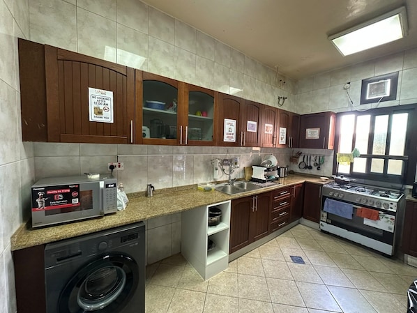 A kitchen with wooden cabinets, a microwave, a washing machine, a sink, and a stove.