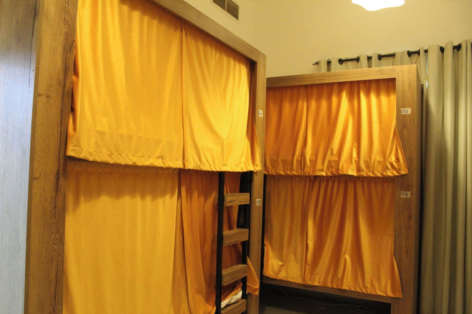 Una habitación con dos camas, cada una cubierta con cortinas amarillas, y una escalera de madera entre ellas.