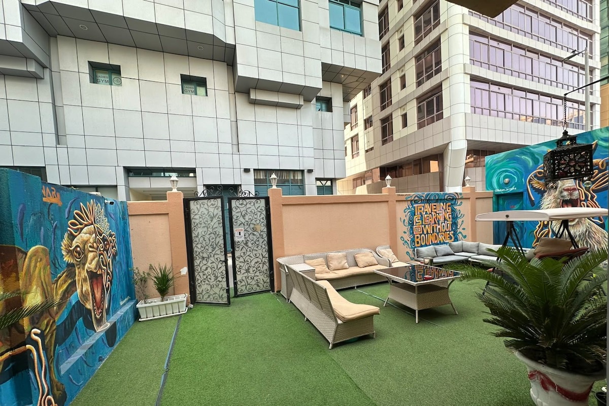 An outdoor seating area with a sofa and a table, surrounded by a mural and a gate.