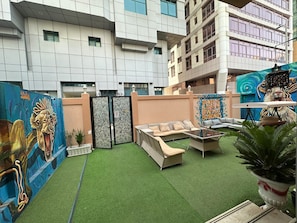 An outdoor seating area with a sofa and a table, surrounded by a mural and a gate.