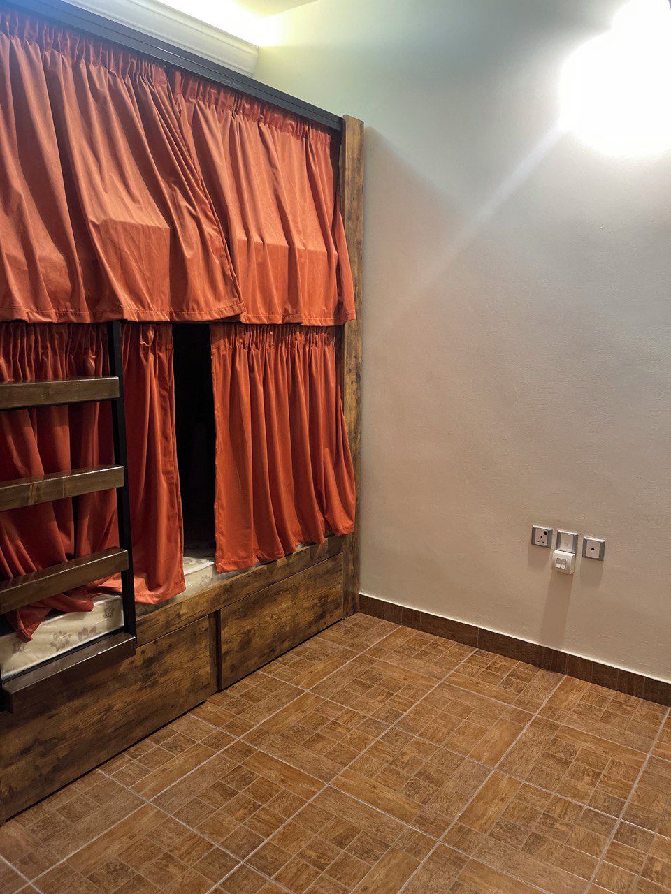 A room with a bunk bed, a wooden ladder, a tiled floor, and a light switch on the wall.