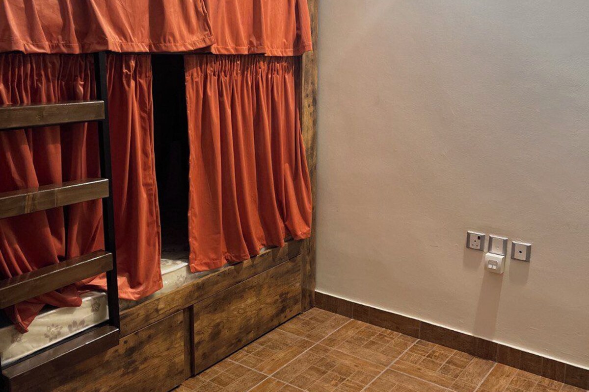 A room with a bunk bed, a wooden ladder, a tiled floor, and a light switch on the wall.