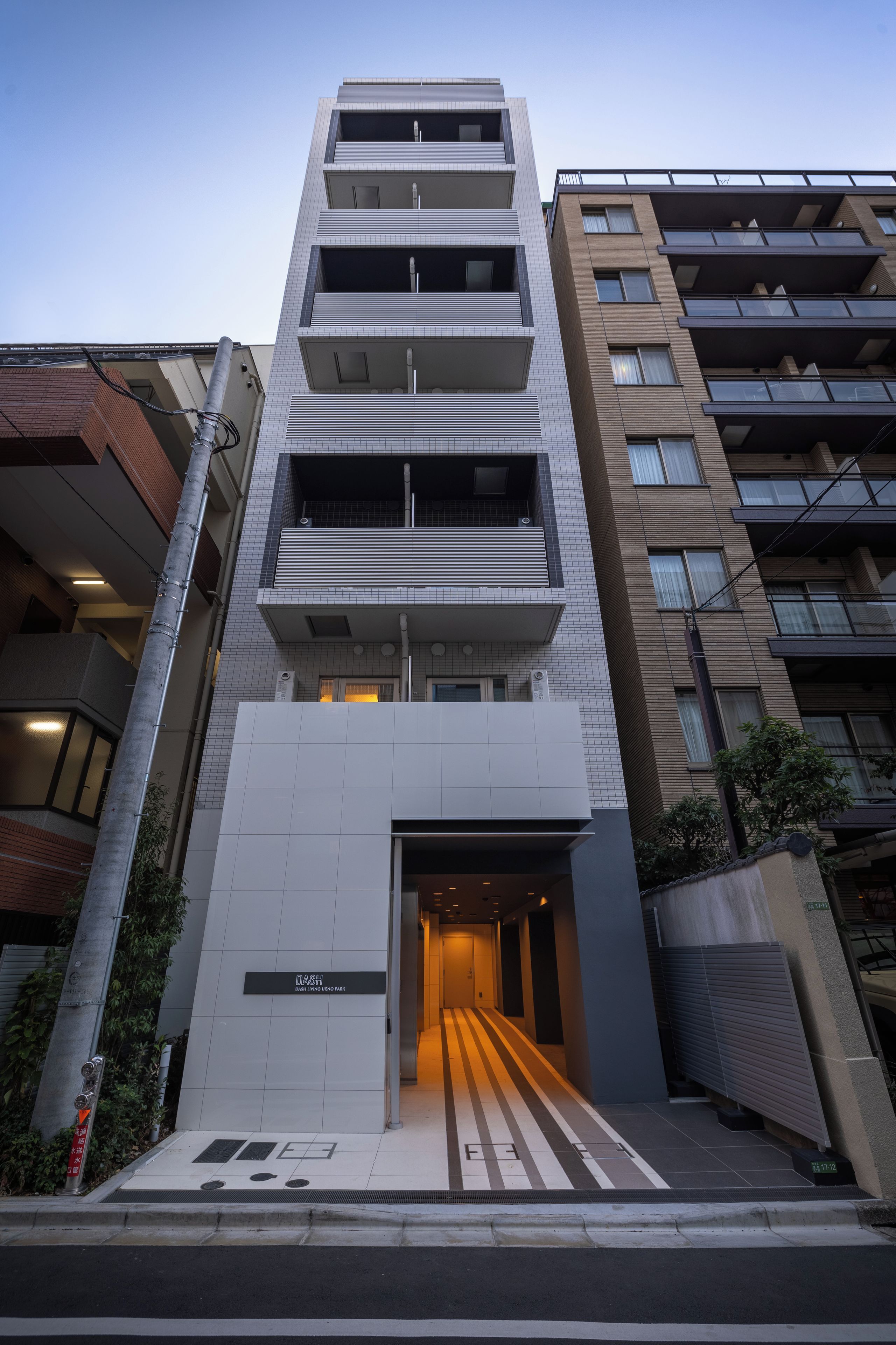 En byggnad med flera våningar och en modern arkitektonisk design, med en framträdande entré och en ramp som leder ner till bottenvåningen.