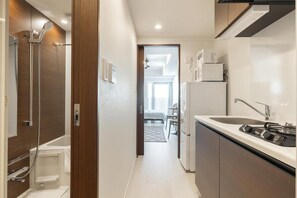 Un pasillo estrecho que da a un dormitorio con ducha, lavamanos y refrigerador.