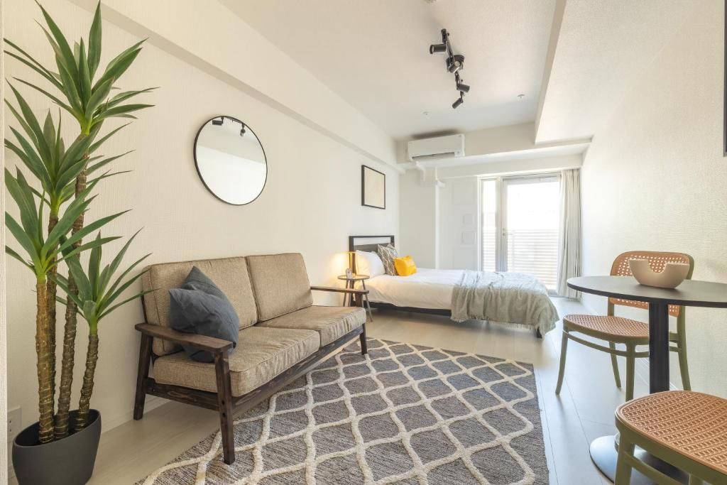 A compact hotel room with a bed, a sofa, a dining table, and a potted plant.