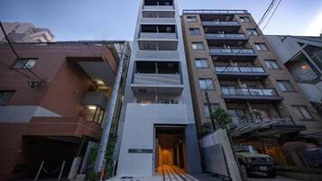 A multi-story residential building with a central entrance, balconies, and a garage with a vehicle parked outside.