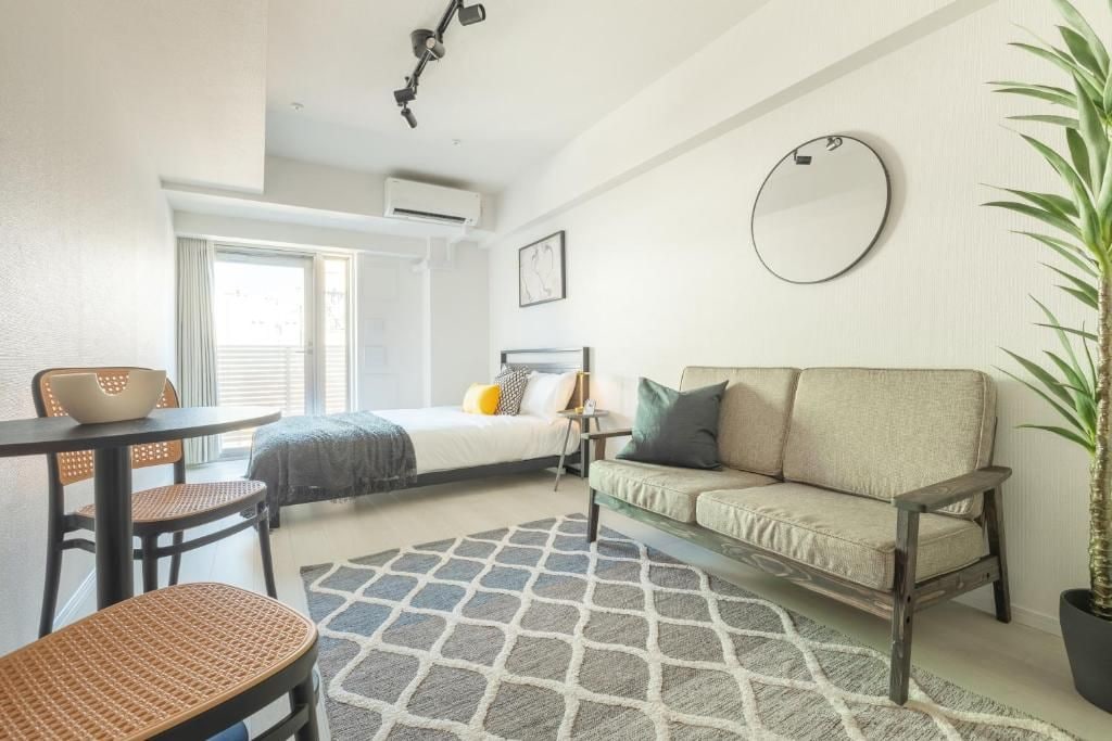A modern hotel room with a bed, a sofa, a dining table, and a potted plant.