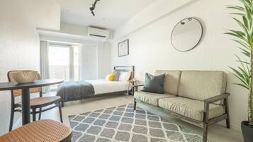 A modern hotel room with a bed, a sofa, a dining table, and a potted plant.