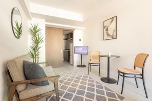 Una sala de estar moderna con un sofá, dos sillones, una mesa de centro, un televisor de pantalla plana, una planta y un cuadro en la pared.